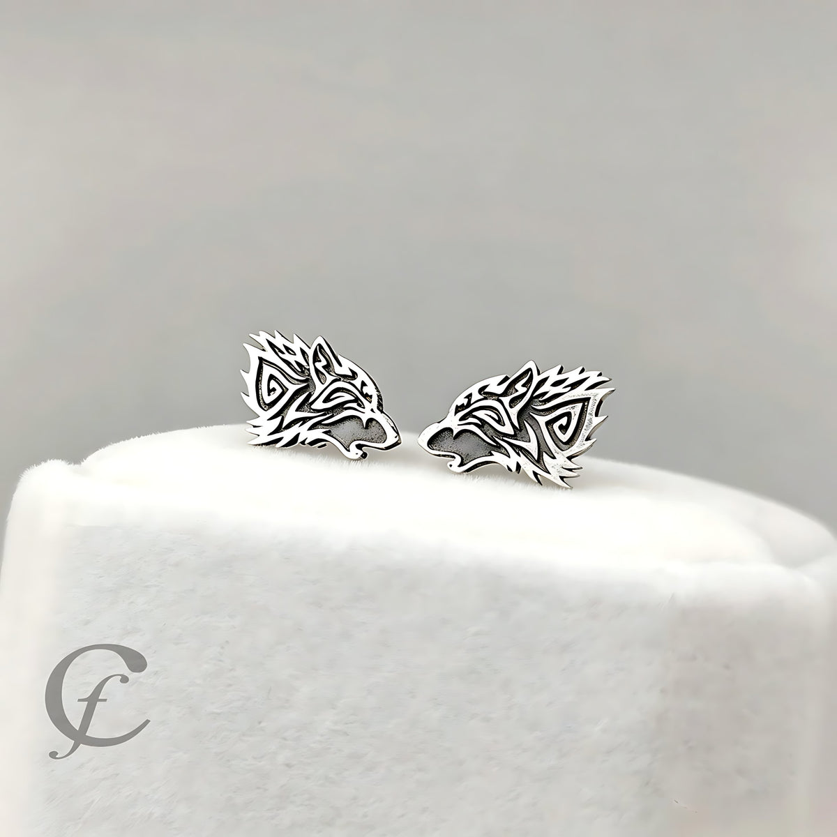 A pair of silver wolf head stud earrings displayed on a white jewelry stand against a soft gray background.