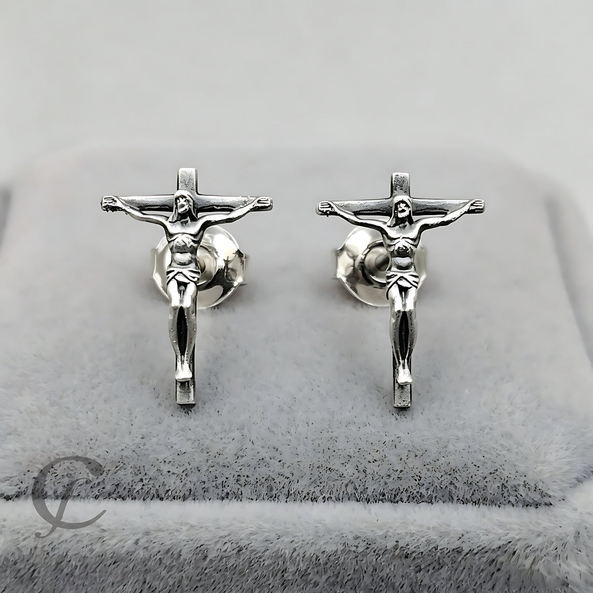 A pair of handcrafted sterling silver crucifix stud earrings displayed on a gray velvet jewelry box.