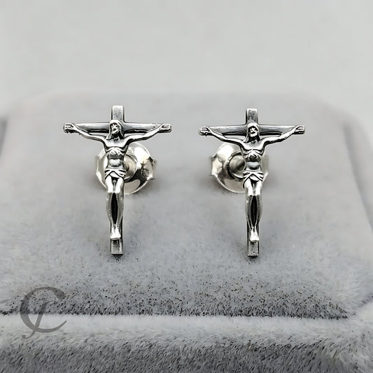 A pair of handcrafted sterling silver crucifix stud earrings displayed on a gray velvet jewelry box.