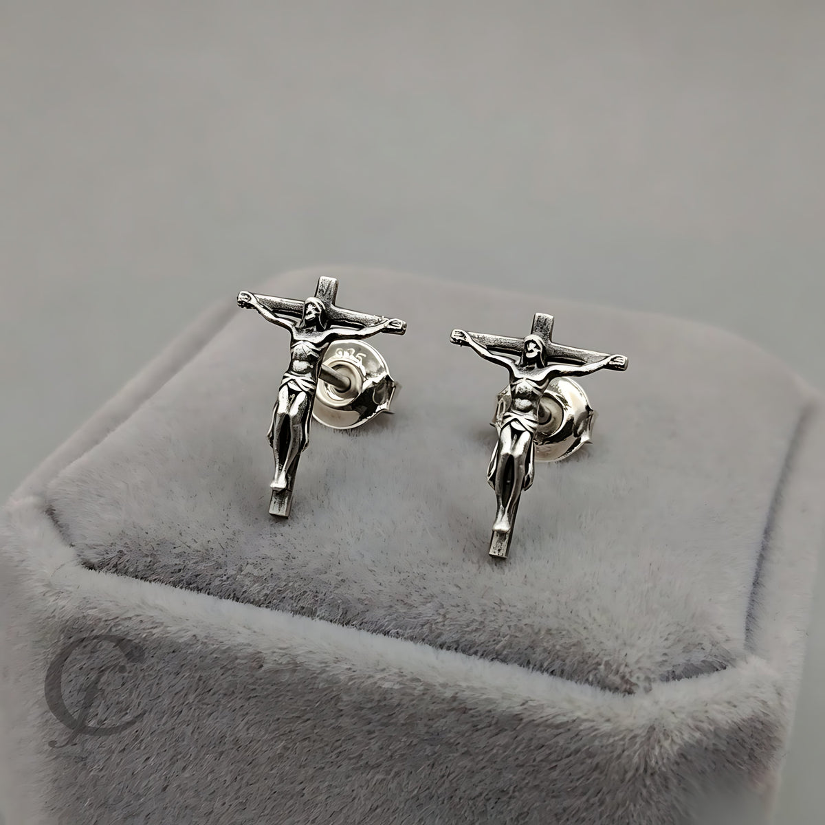 A pair of silver crucifix stud earrings displayed on a gray velvet jewelry box.