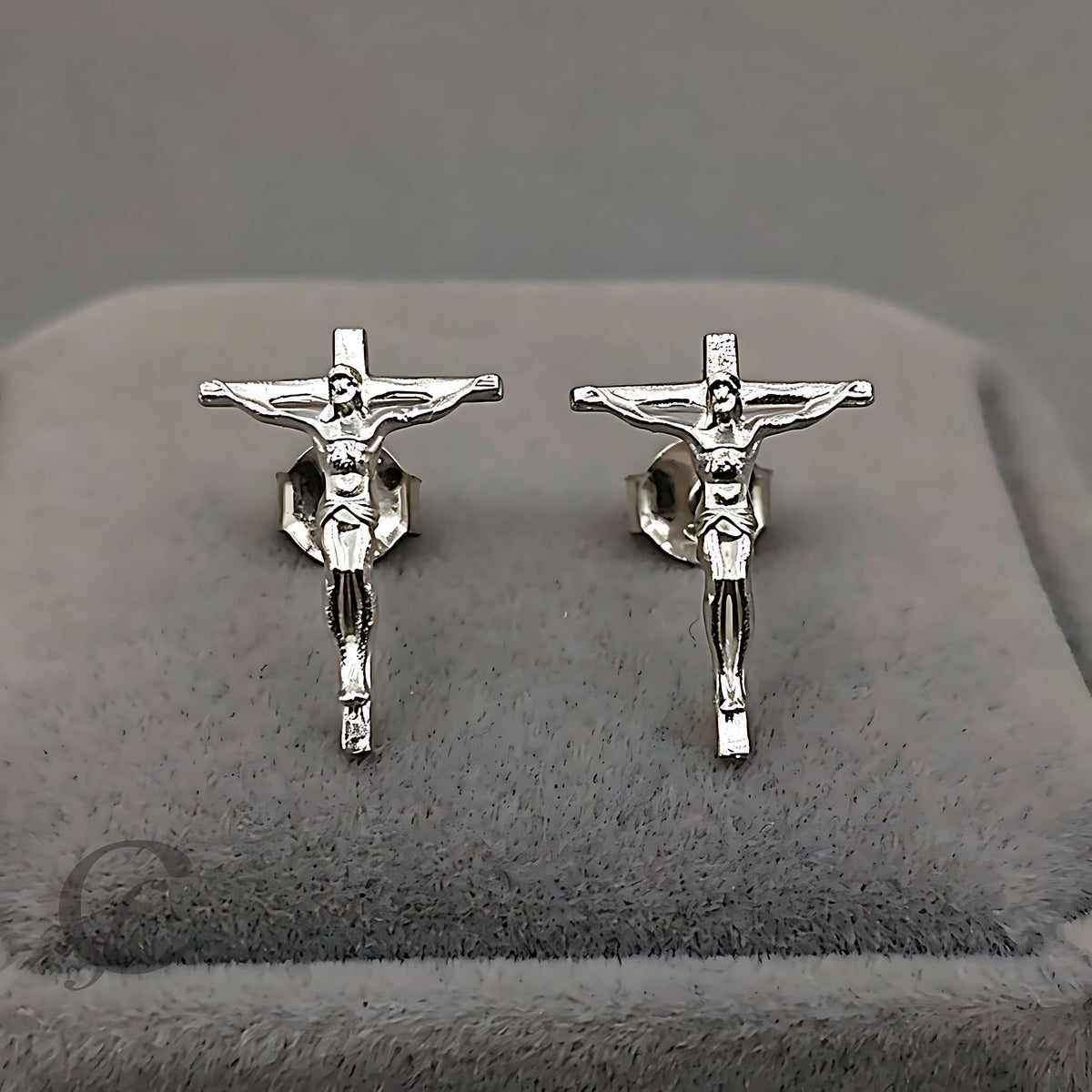 A pair of silver crucifix stud earrings displayed on a gray velvet jewelry box.