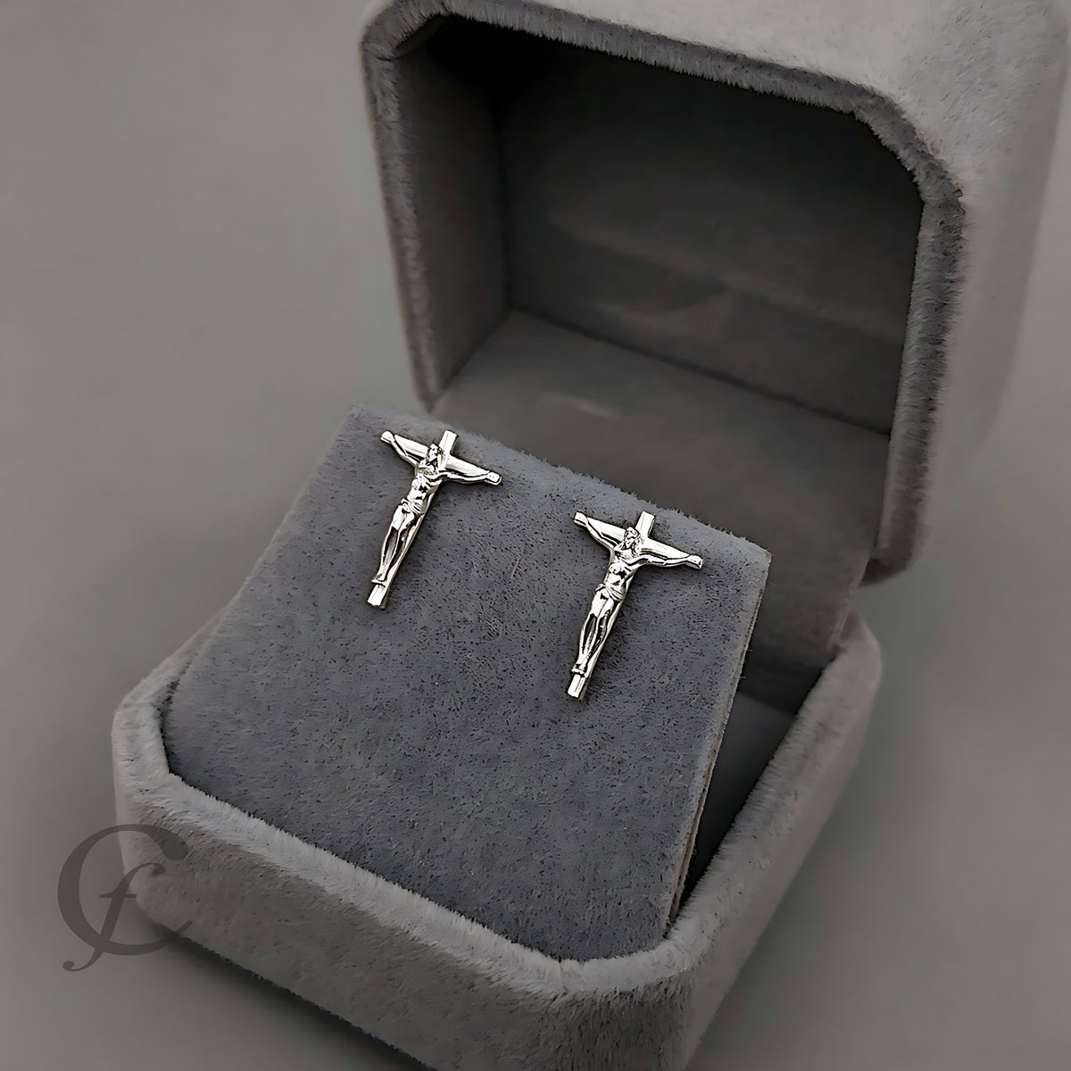 A pair of silver crucifix earrings displayed on a gray velvet jewelry box.