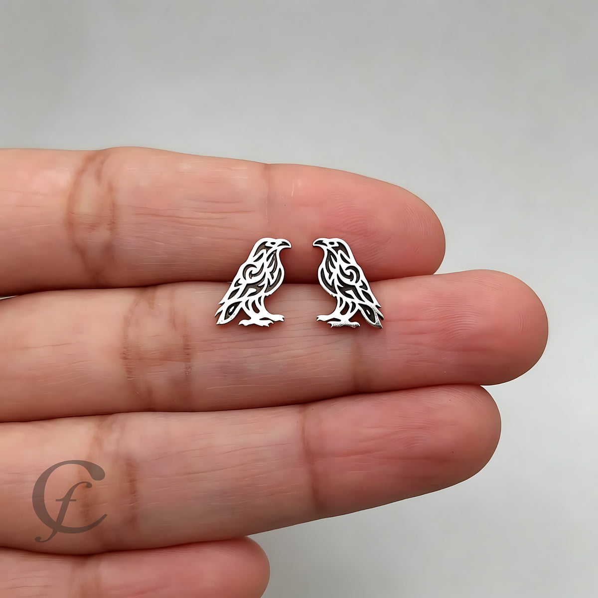 Silver bird-shaped earrings held between two fingers against a neutral background