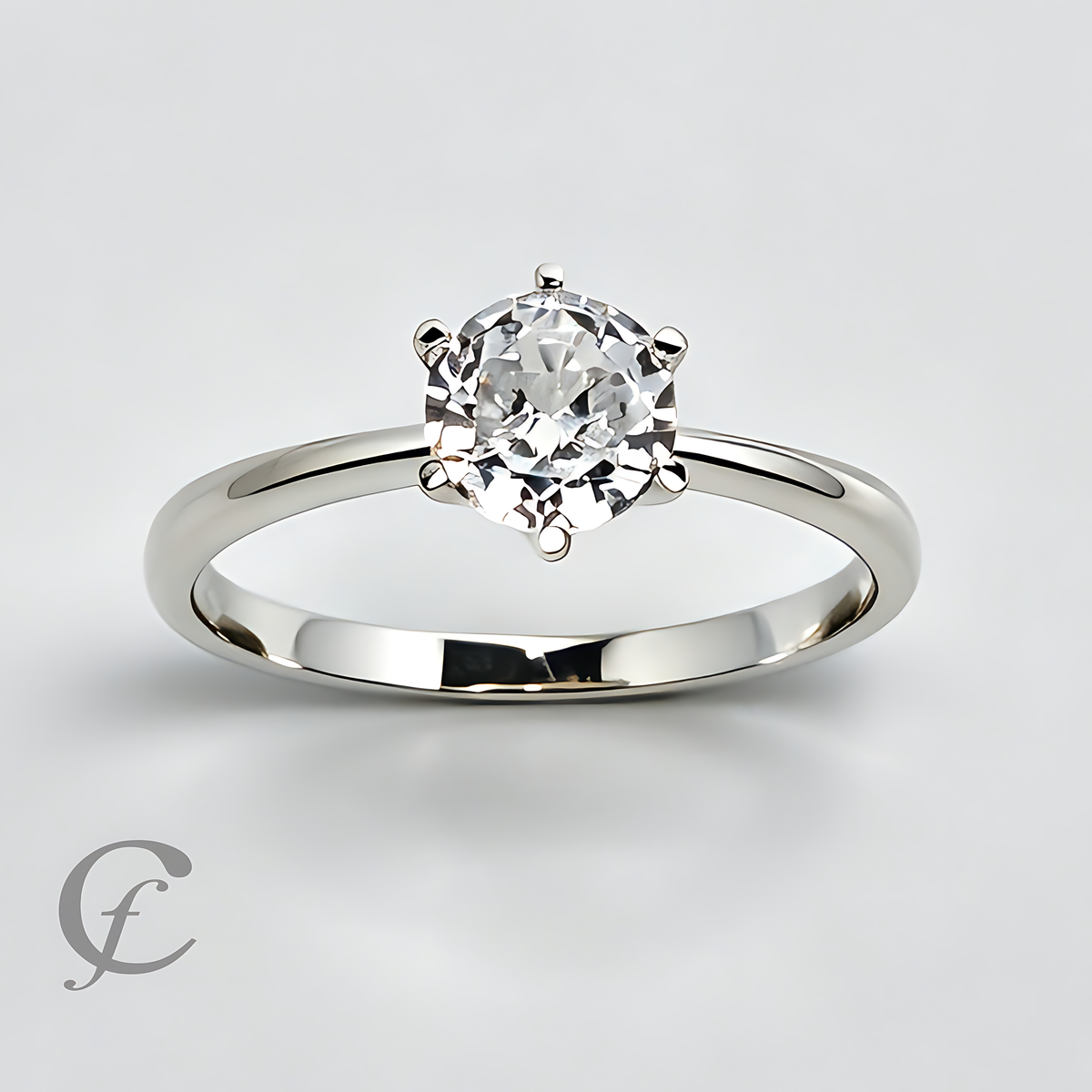 A classic solitaire engagement ring featuring a round brilliant-cut diamond set in a polished white gold or platinum band, shown on a light gray background with a watermark logo in the lower-left corner.