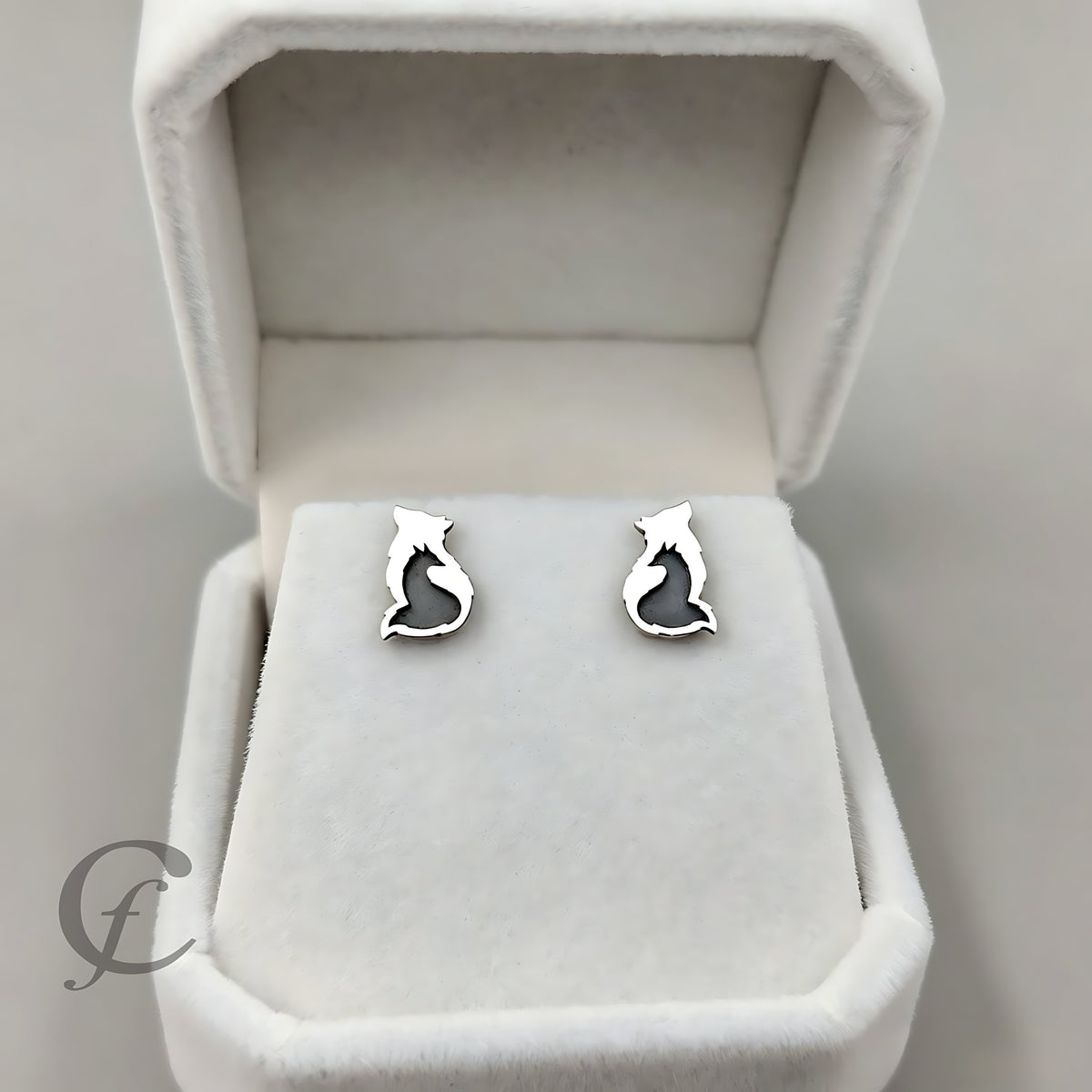 A pair of silver stud earrings shaped like Wolf & Fox Silhouette silhouettes, displayed on a white velvet jewelry box.