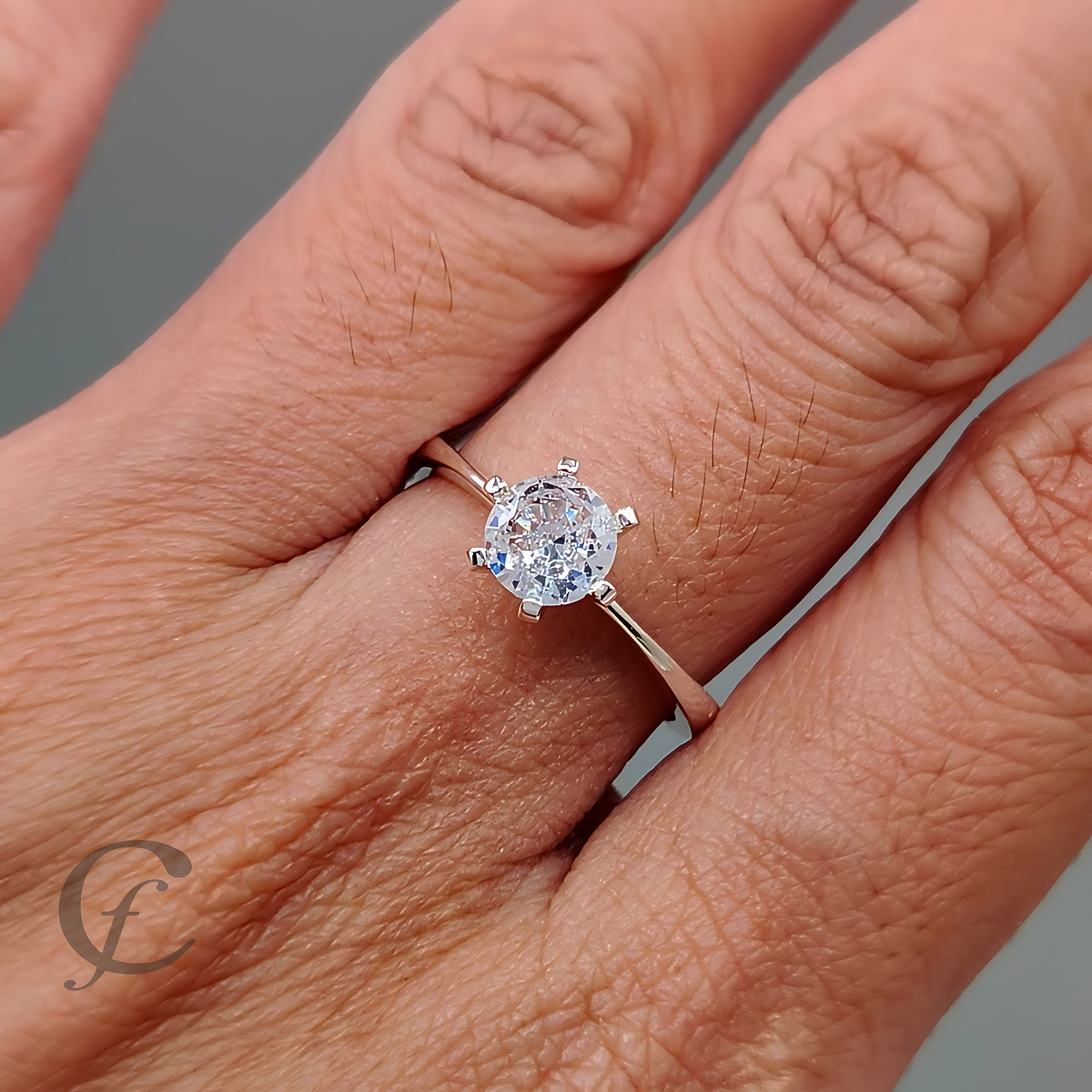A close-up of a hand wearing a solitaire engagement ring with a round brilliant-cut clear gemstone in a silver-toned setting on a slim band.