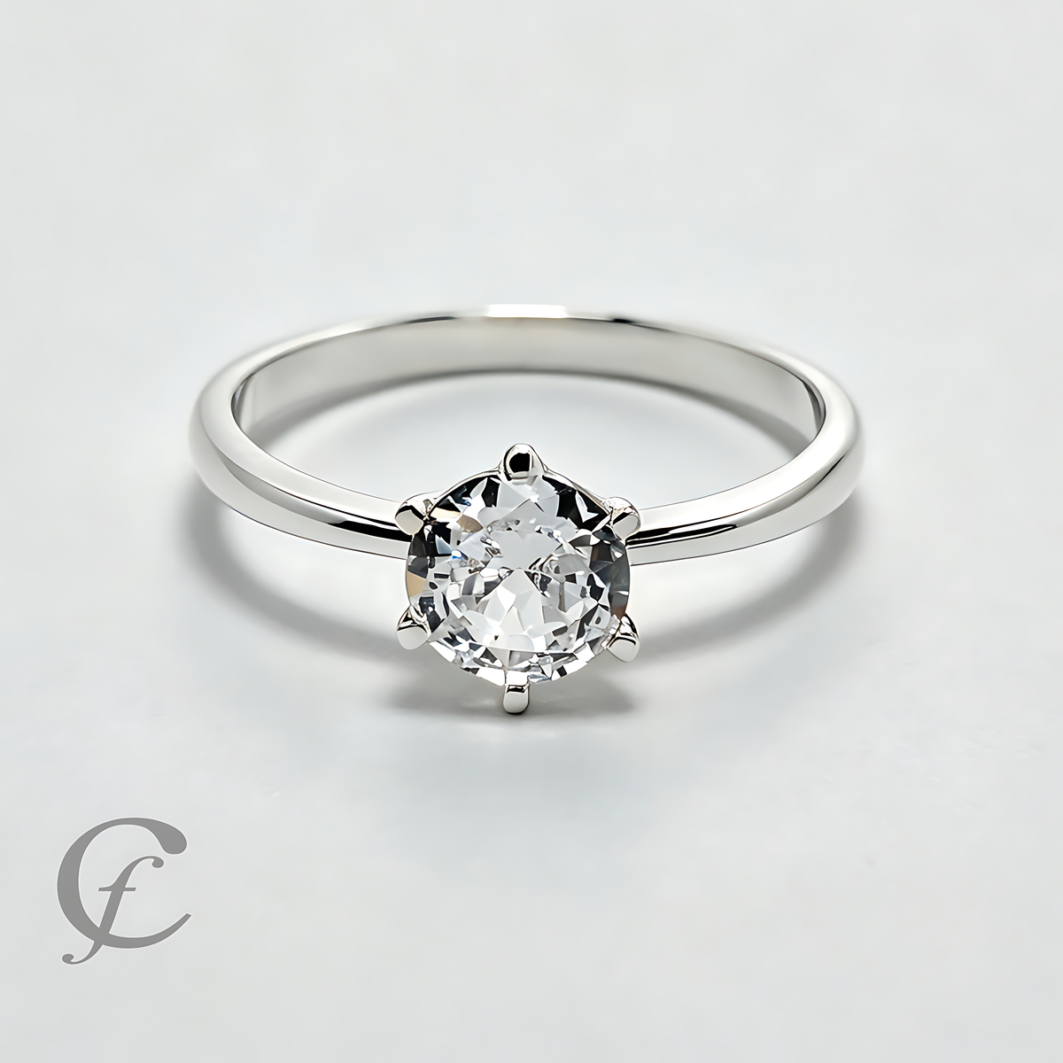 A classic solitaire engagement ring featuring a round brilliant-cut clear gemstone in a six-prong setting on a polished silver-colored band, photographed on a light gray background.