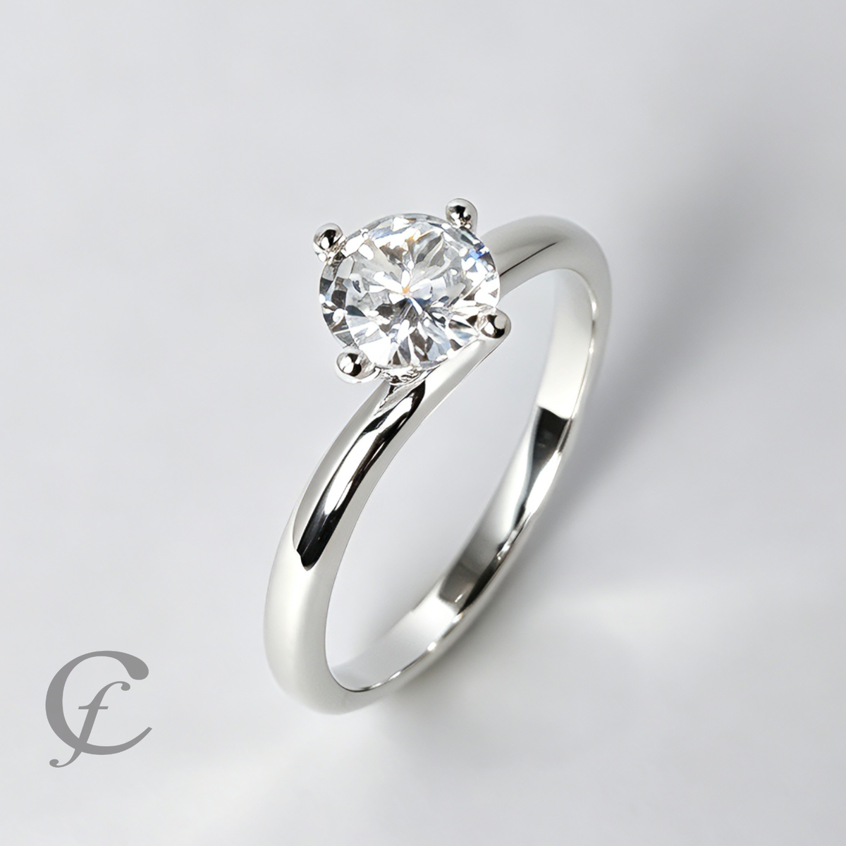 A classic solitaire engagement ring featuring a round brilliant-cut diamond set in a polished silver-colored band, photographed on a clean light gray background with a subtle watermark in the lower-left corner.