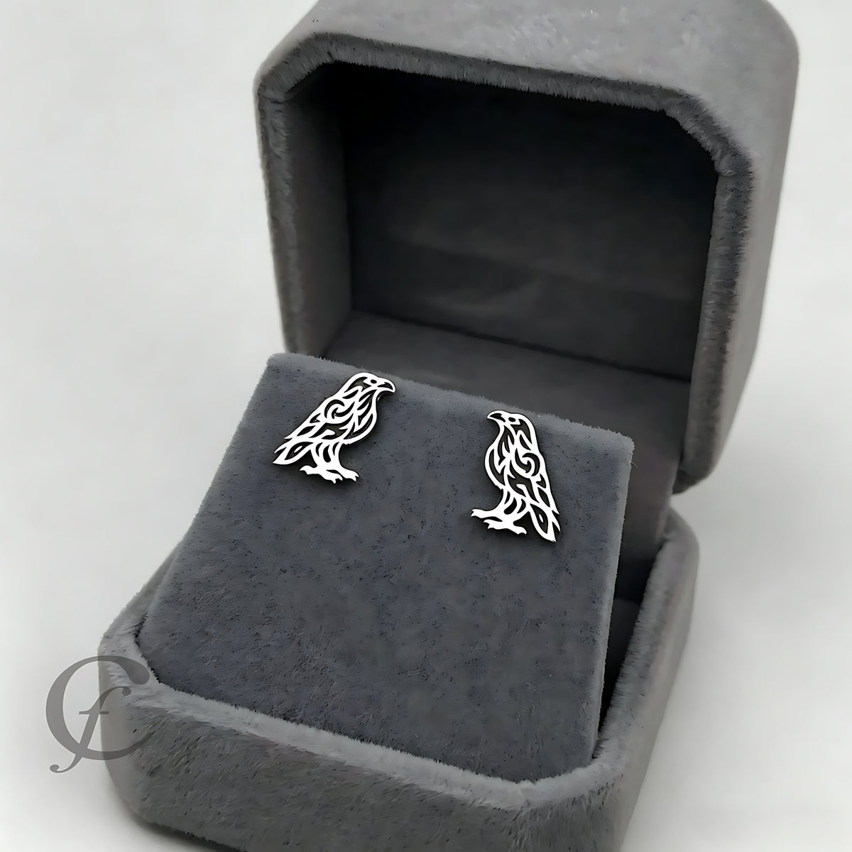 A pair of silver bird stud earrings displayed on a gray velvet jewelry box against a light gray background.