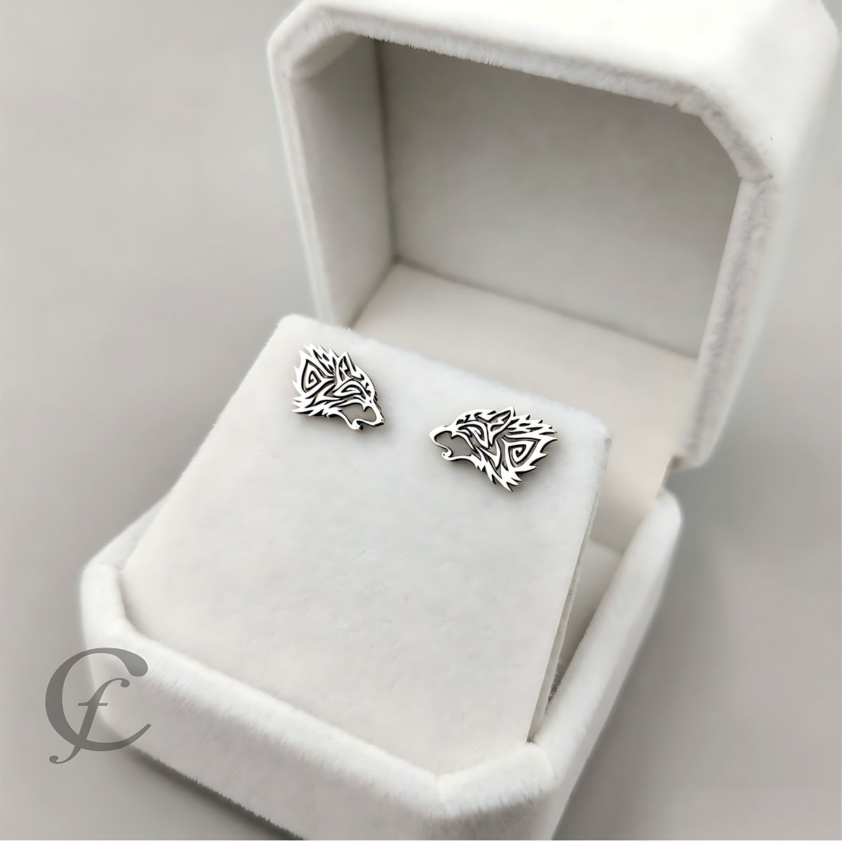 Silver Wolf-shaped earrings in an open jewelry box on a light gray background
