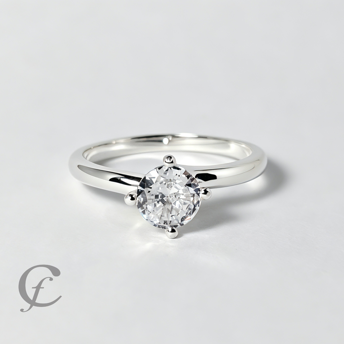 A classic solitaire engagement ring featuring a round brilliant-cut diamond set in a polished silver four-prong setting on a matching silver band, photographed on a clean light gray background.